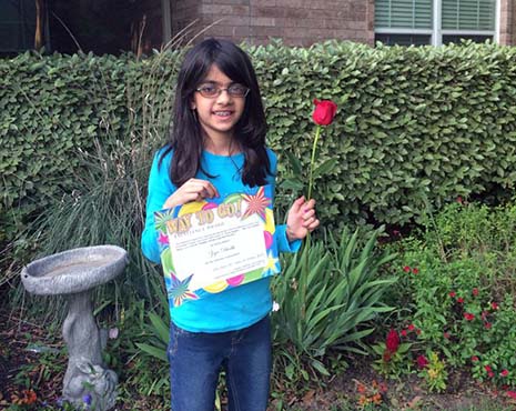 Zoya Dhedhi holding red rose and certificate for excellence for teaching and performance.